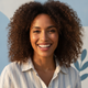 A diverse woman, mid-30s, smiles warmly at the camera, conveying happiness and trust. The background is a soft, blurred mix o